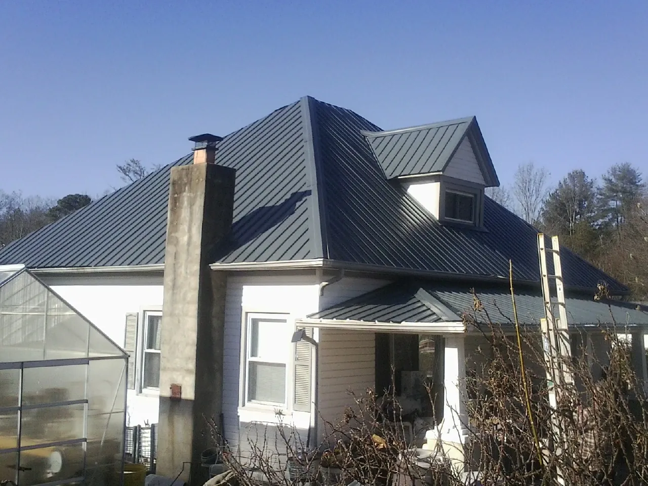 Dark blue standing seam metal roof on a white farmhouse with dormer — Slate & Tile Roof Repair by Roofing Brothers in Manlius