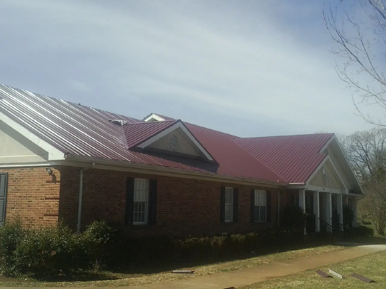 Red metal roof with gabled entries on a long brick building, from a Hail Damage Roof Repair job in Manlius