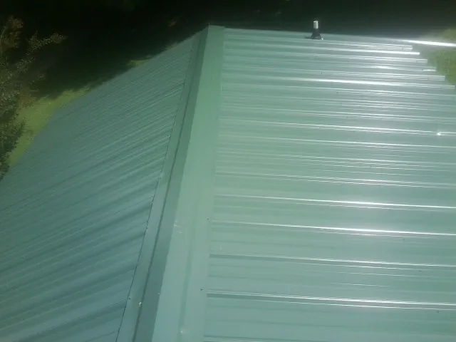 New green metal panels meeting at the ridge of a roof — Flat Roof Repair work by our crew in Manlius