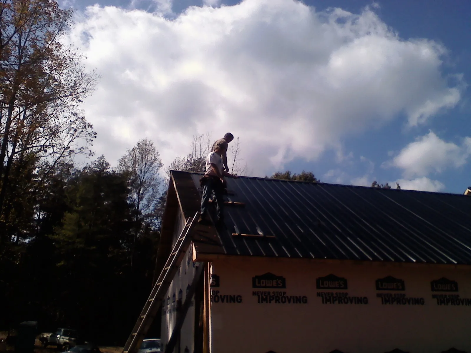 Roofer fastening dark metal panels high against a cloudy sky, from a Roof Inspection job in Manlius
