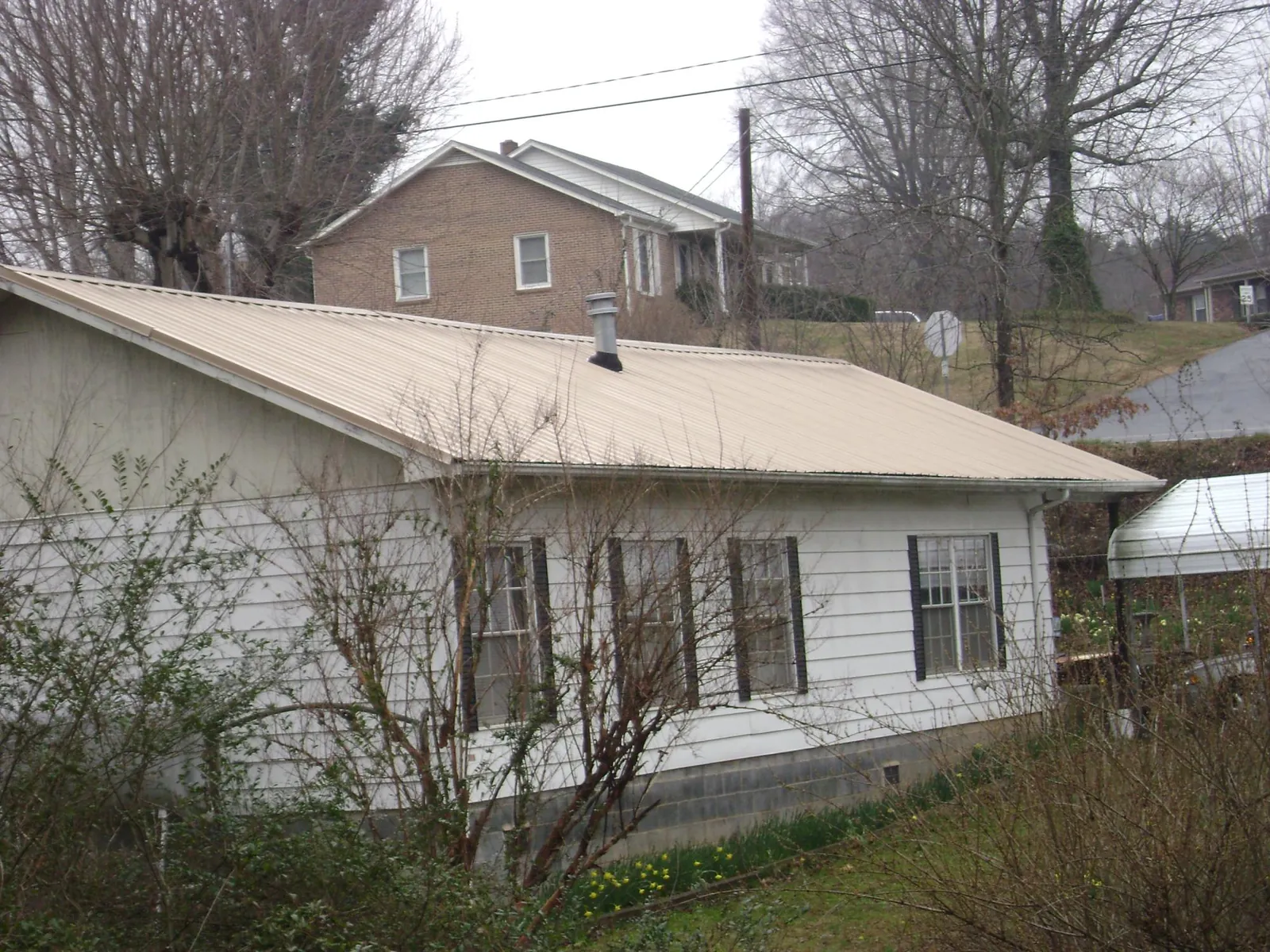 Tan metal roof on a white sided house set into a hillside — Commercial Roofing by Roofing Brothers in Manlius