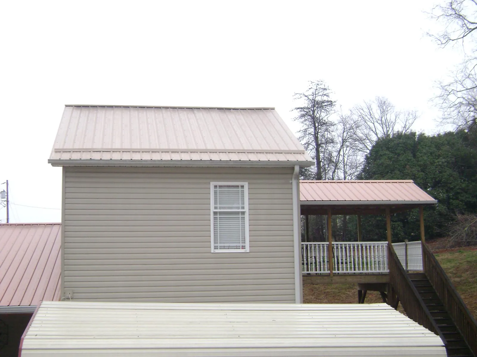 Tan metal roofs on a two story addition and attached porch, from a Roof Replacement job in Manlius